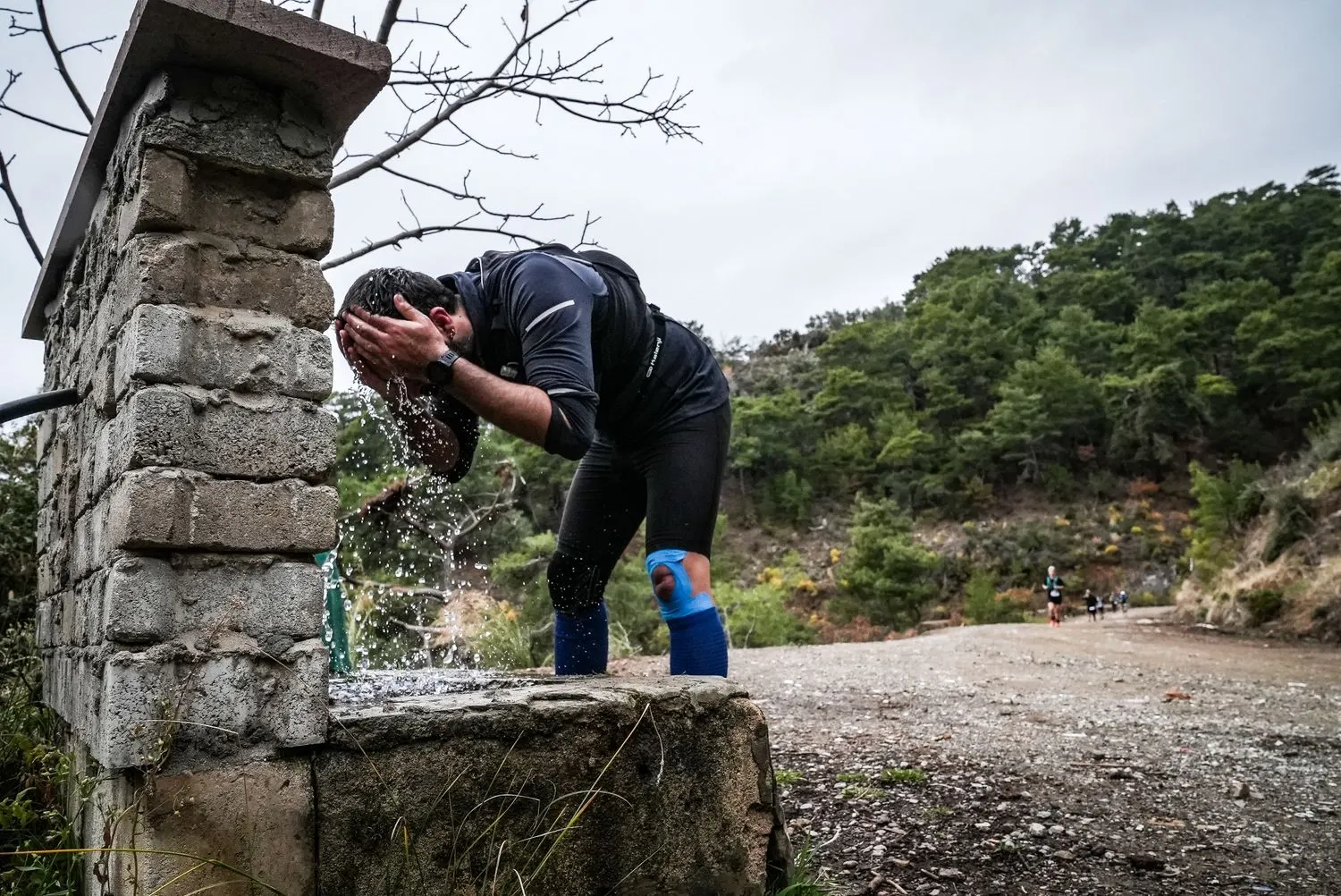 Un coureur se passe de l'eau sur le visage à une fontaine en pierre.