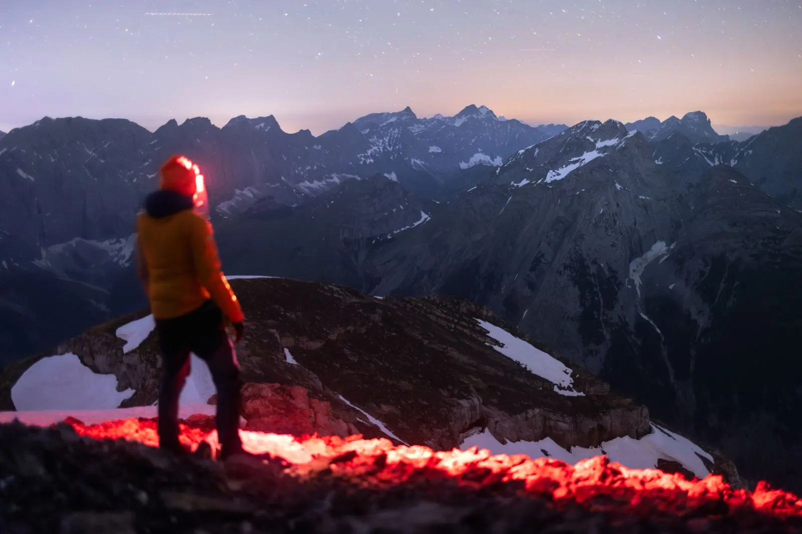 Une personne avec une frontale rouge, de nuit, face à une chaîne de montagnes.