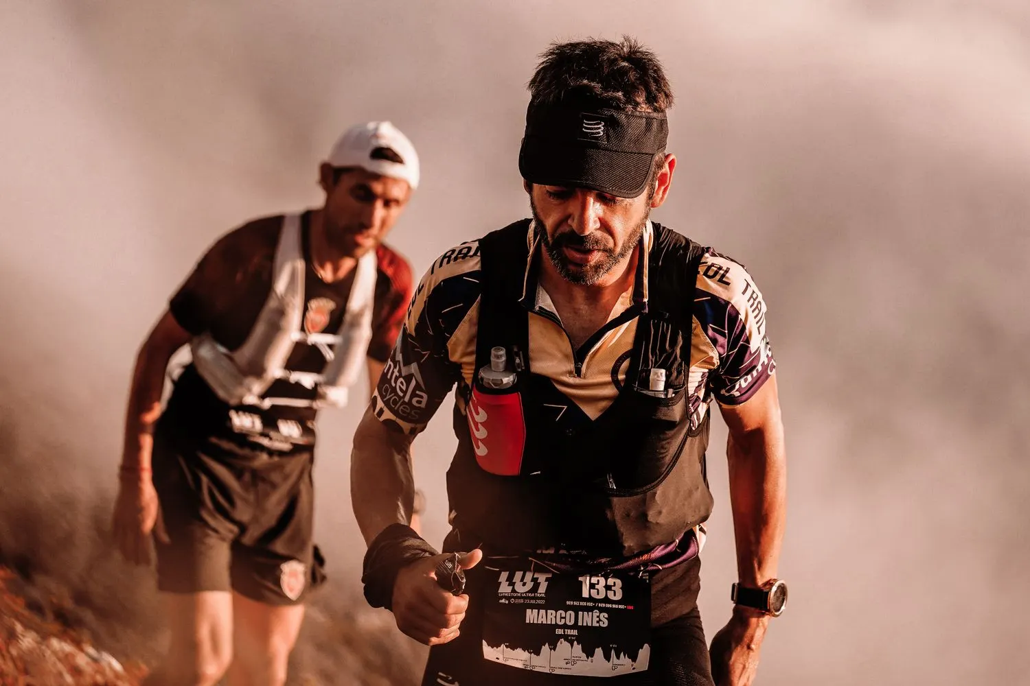 Deux coureurs en montée, concentrés, dans la brume.